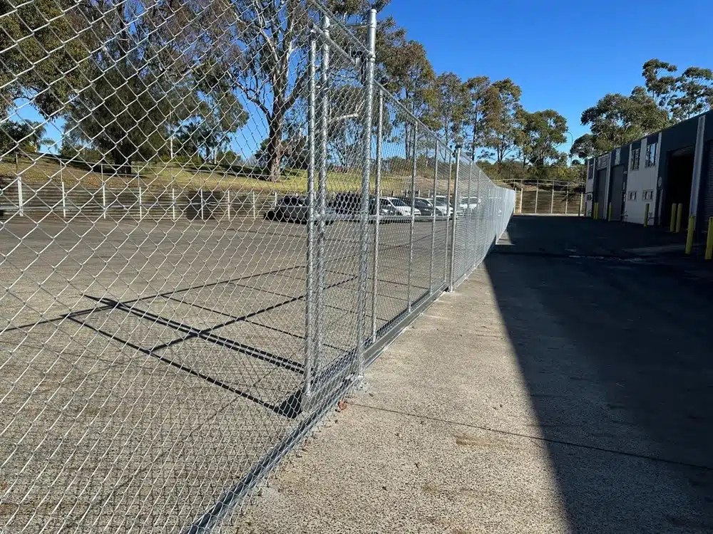 Chain-link fence with metal posts enclosing a paved industrial area beside a warehouse.
