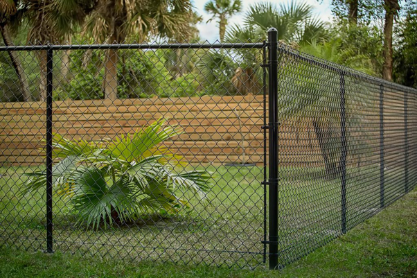 Black chain wire fencing enclosing a commercial outdoor area with grass and timber fencing in the background